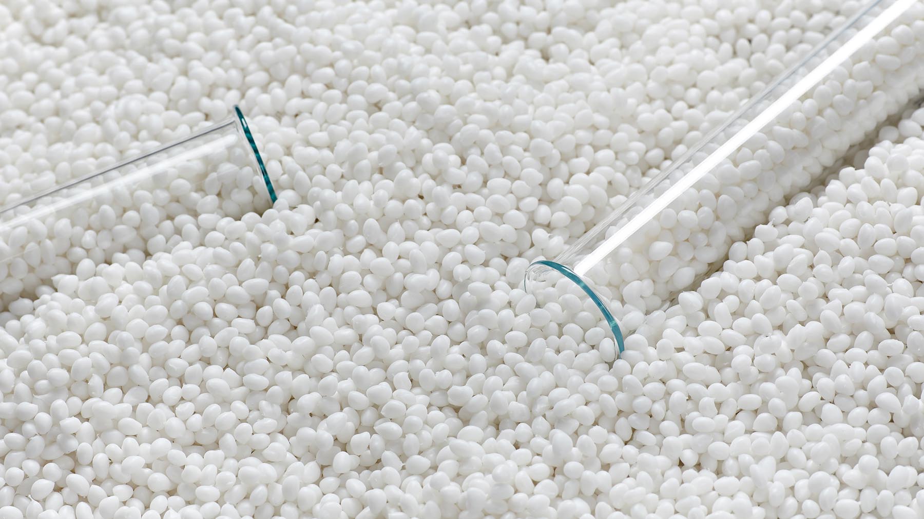 Closeup of a granule of white plastic polymer with laboratory glassware. Conceptual image.